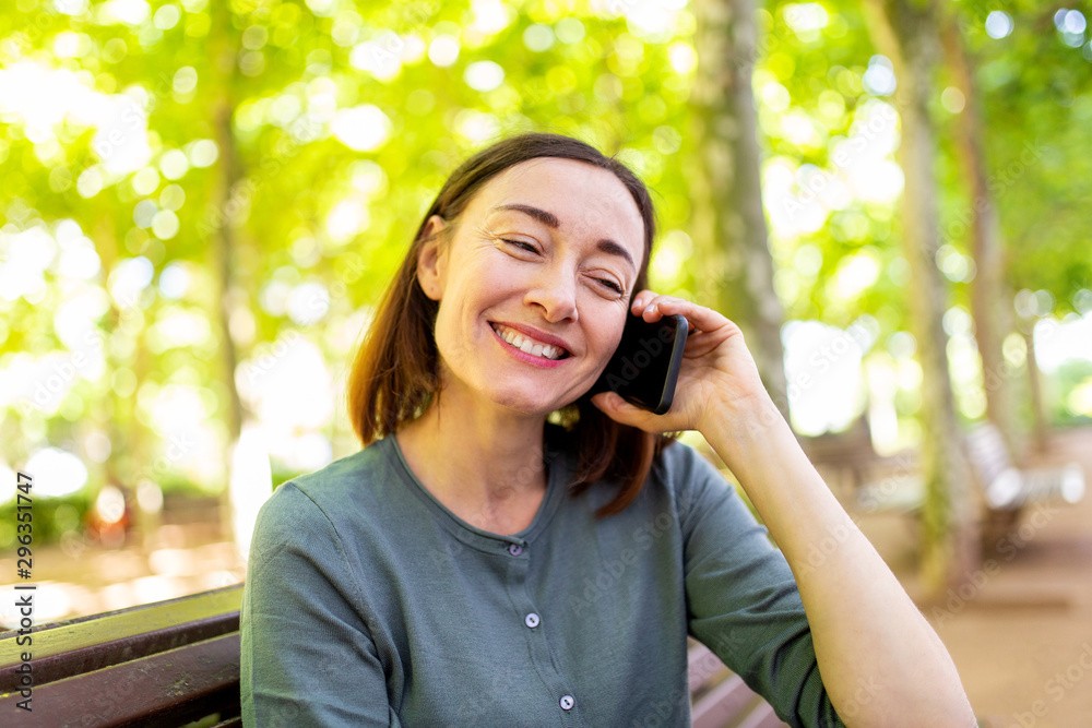 smiling middle aged woman sitting in park talking with cellphone smiling middle aged woman sitting in park talking with cellphone