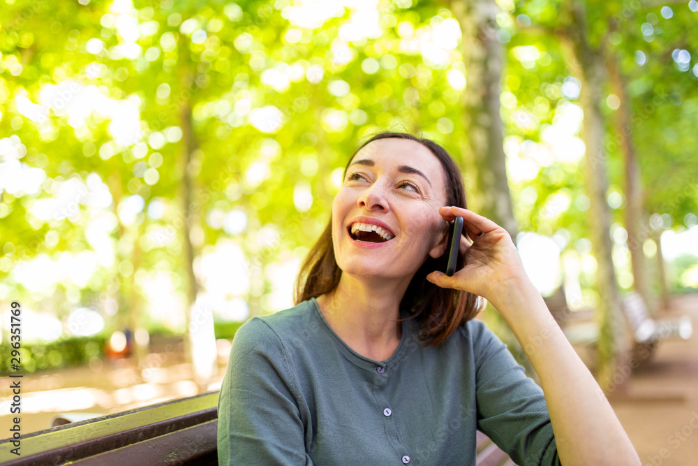 smiling middle aged woman sitting in park talking with mobile phone smiling middle aged woman sitting in park talking with mobile phone