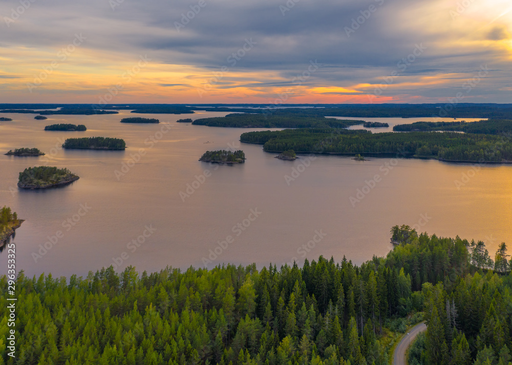 Aerial view of of small islands on a blue lake Saimaa. Landscape with drone. Blue lakes, islands and green forests from above on a cloudy summer sunset. Lake landscape in Finland.