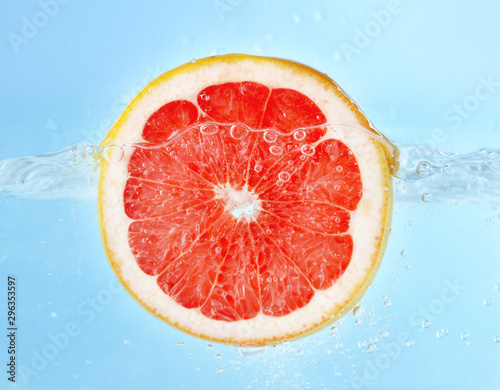 Falling of grapefruit piece into water on color background