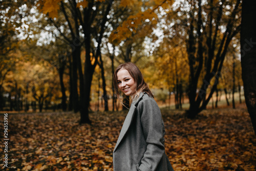 Long-haired woman in a gray coat and white jacket posing in the autumn forest. © velimir