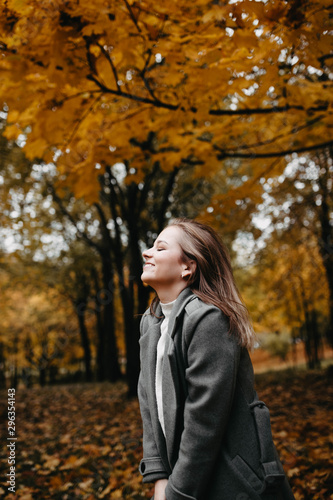 Autumn portrait of a young girl in an autumn park in a gray coat. Posing at a photo shoot in nature. © velimir