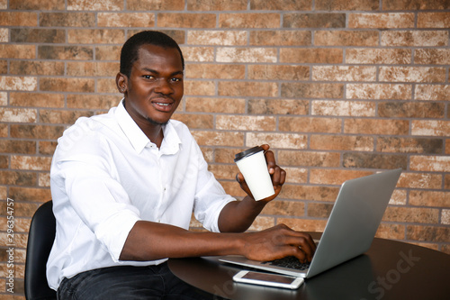 Handsome African-American man drinking coffee while working on laptop in cafe