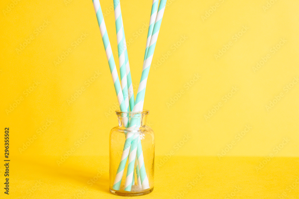 pile of paper striped white and green drinking straws for party in clear glass small bottle on yellow background pile of paper striped white and green drinking straws for party in clear glass small bottle on yellow background