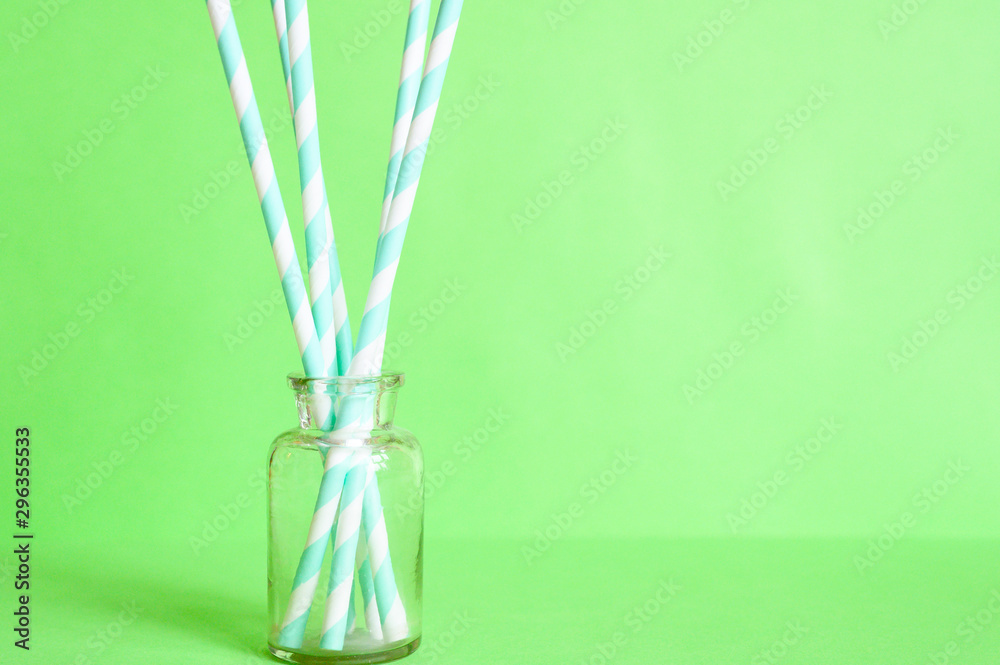 pile of paper striped white and green drinking straws for party in clear glass small bottle on green background. space for text pile of paper striped white and green drinking straws for party in clear glass small bottle on green background. space for text