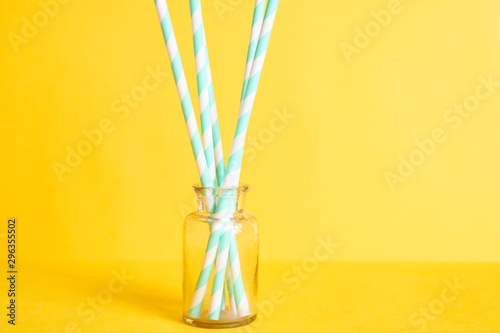 pile of paper striped white and green drinking straws for party in clear glass small bottle on yellow background © Ksenia
