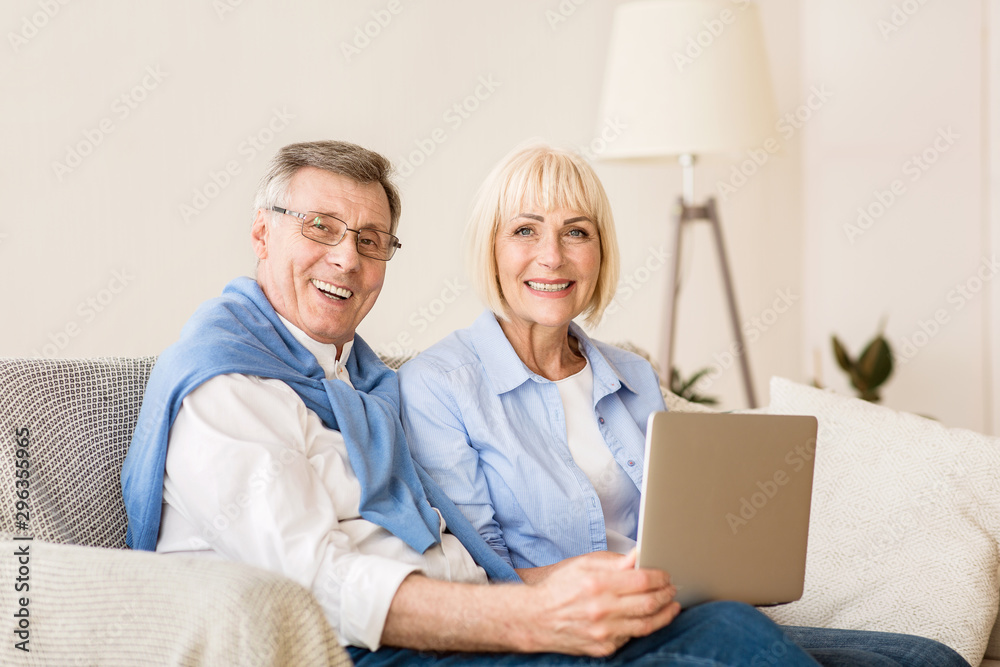 Joyful elderly couple with laptop smiling to camera Joyful elderly couple with laptop smiling to camera