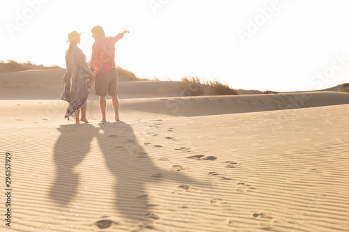 Back view of young couple standing on sandy beach. Husband and wife talking and pointing on seashore during vacation. Vacation concept