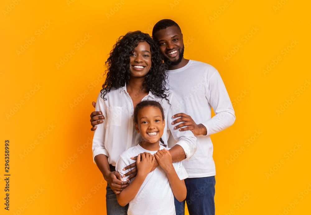 Happy Family Of Three Hugging And Posing Over Yellow Background