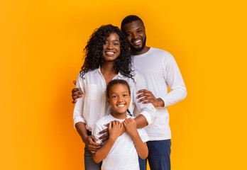 Happy Family Of Three Hugging And Posing Over Yellow Background