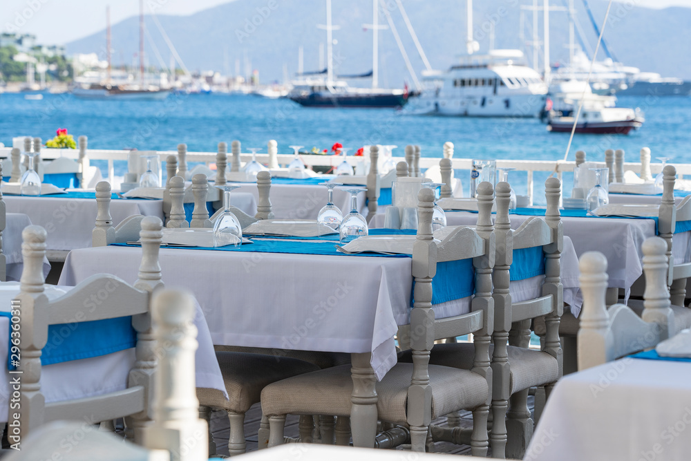 Fototapeta premium Elegant table setting with fork, knife, wine glass, white plate and blue napkin in restaurant . Nice dining table set with arranged silverware and napkins for dinner