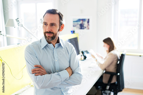 Portrait of confident businessman in office with employee in background