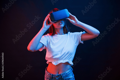 Amazing modern technologies. Young woman using virtual reality glasses in the dark room with neon lighting