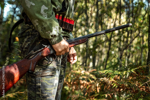 A hunter with a gun in his hands in hunting clothes in the autumn forest close-up. The hunting period, the fall season is open, the search for prey.