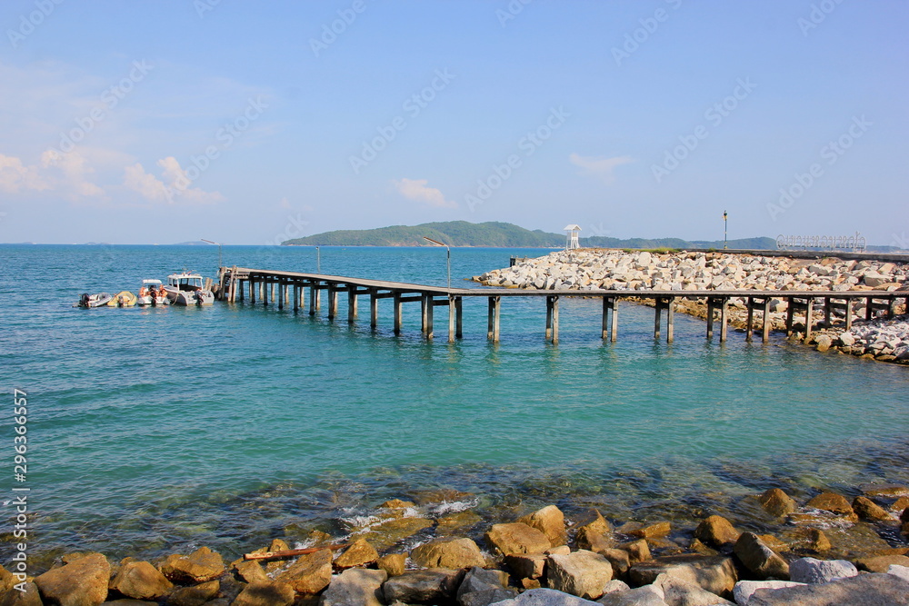 A wooden bridge at sea and a boat moored at the dock on a clear day,Rayong Thailand.