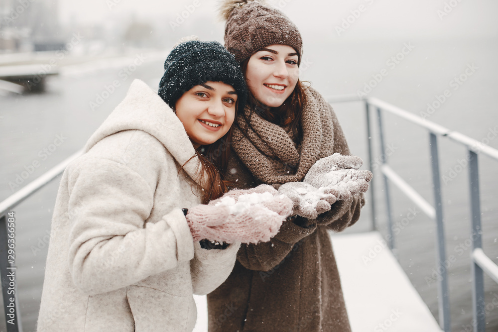 two bright and merry girls walking in the frozen snowy park near water two bright and merry girls walking in the frozen snowy park near water