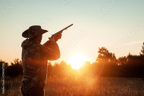 Silhouette of a hunter in a cowboy hat with a gun in his hands on a background of a beautiful sunset. The hunting period, the fall season is open, the search for prey.
