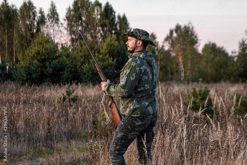 Hunter man in camouflage with a gun during the hunt in search of wild birds or game on the background of the autumn forest. Autumn hunting season. The concept of a hobby, killing. Hunter man in camouflage with a gun during the hunt in search of wild birds or game on the background of the autumn forest. Autumn hunting season. The concept of a hobby, killing.