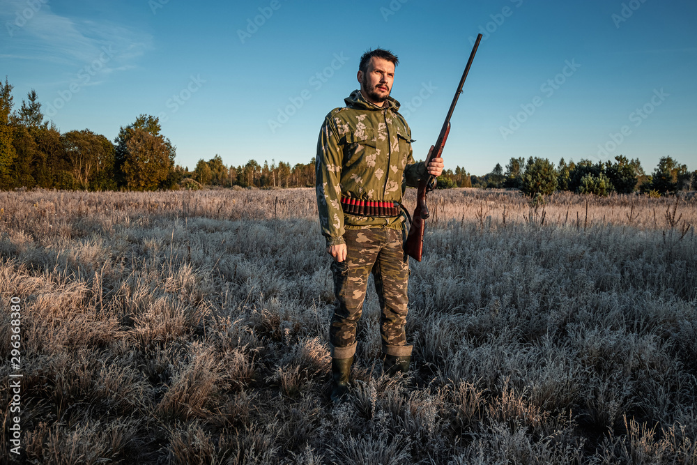 Hunter man in camouflage with a gun during the hunt in search of wild birds or game on the background of the autumn forest. Autumn hunting season. The concept of a hobby, killing. Hunter man in camouflage with a gun during the hunt in search of wild birds or game on the background of the autumn forest. Autumn hunting season. The concept of a hobby, killing.
