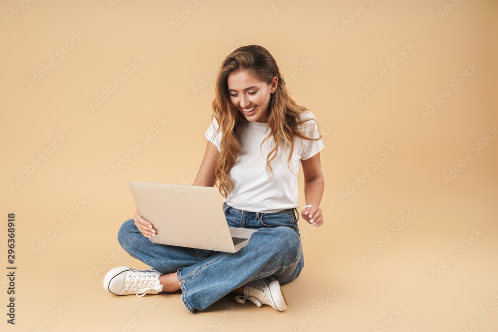 Image of smiling woman using silver laptop while sitting on floor Image of smiling woman using silver laptop while sitting on floor