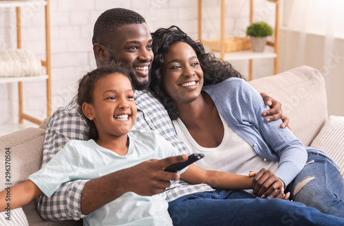 African American Family Of Three Sitting On Sofa Watching Television