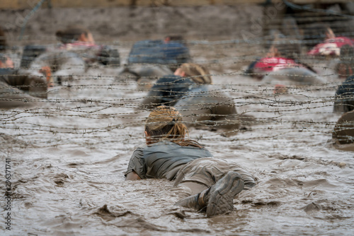 A woman crawling under barbed wire at a mud run