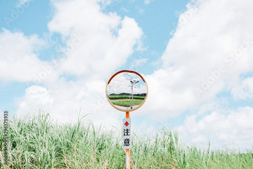 Reflection of road in curved mirror over caution sign in field