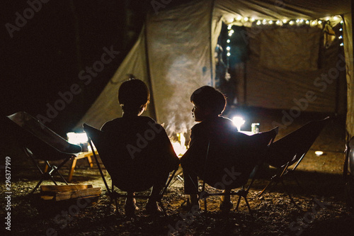 Rear view of siblings sitting near campfire at night