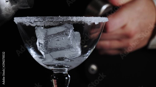 Close up of a bartender shaking and pouring a fresh classic yellow cocktail drink in a sugared glass filled with ice and lemon slice