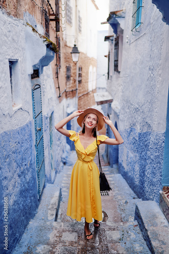 Colorful traveling by Morocco. Young woman in yellow dress walking in  medina of  blue city Chefchaouen. © luengo_ua