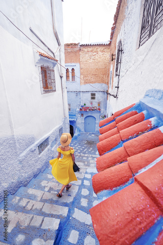 Colorful traveling by Morocco. Young woman in yellow dress walking in medina of blue city Chefchaouen.