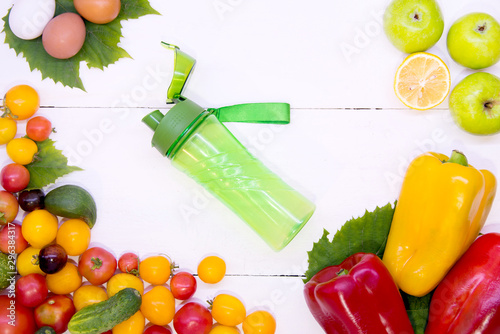 Smoothies with vegetables. Sports green bottle on a white wood texture background top view around different vegetables. Sports nutrition and diet. The concept raw food detoxification.