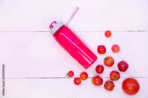 Pink tomato smoothie. Sports pink bottle on a white background top view. Sports nutrition and diet. Detox Raw Food Concept. Tomatoes around a pink plastic bottle
