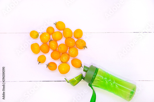 Yellow tomato smoothie. Sports green bottle on a white background top view. Sports nutrition and diet. Detox Raw Food Concept. Tomatoes spilling out of a green plastic bottle