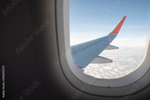 View from inside airplane window. Looking outside at the airplane wing seeing clouds and a blue sky.