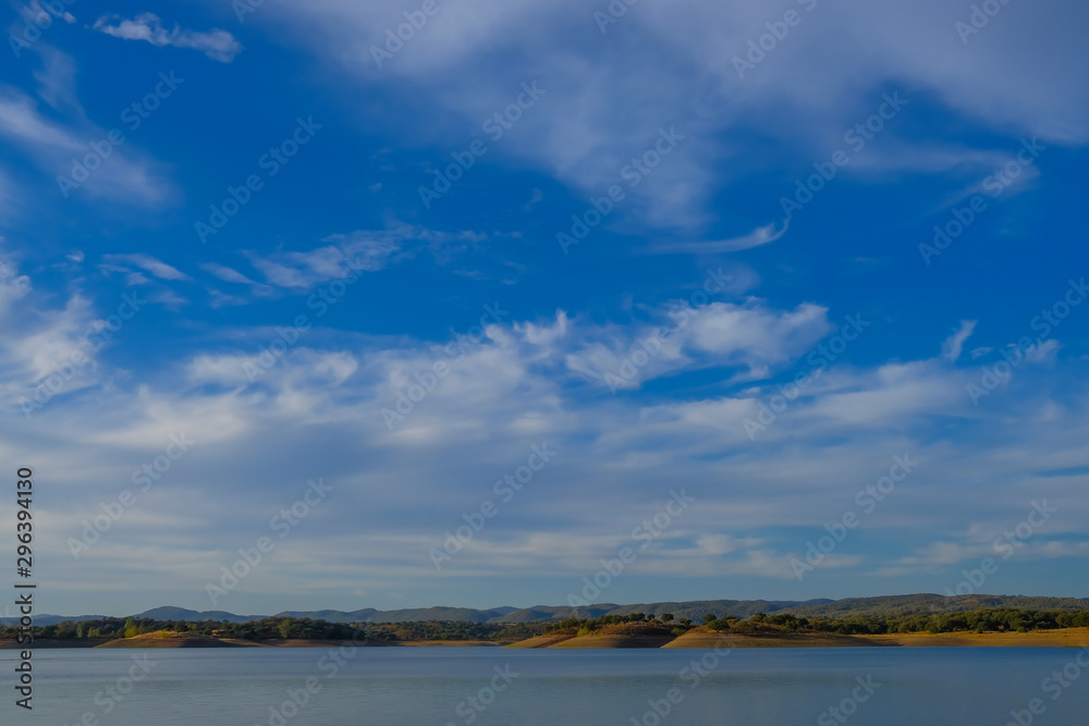 Blue sky with some white clouds over a lake with mountains in the background Blue sky with some white clouds over a lake with mountains in the background