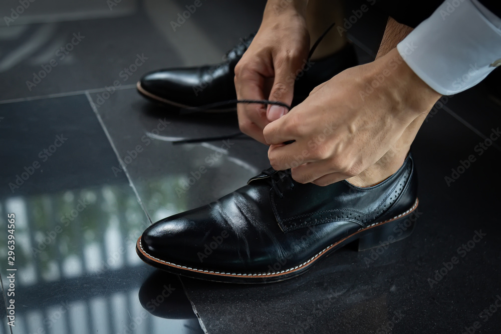 Business man in a black suit tie a black leather shoe on black floor. The hands of a business man who is shoelace.