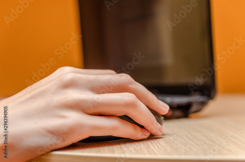 Female hand with a mouse on a wooden table next to a laptop