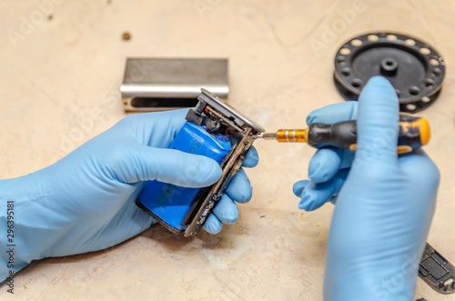 Male hands in blue gloves repair an electronic cigarette on a wooden light table close up