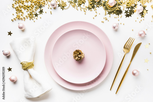 Christmas table setting with pink dishware, golden silverware and party decorations on white background. Top view. Xmas dinner.