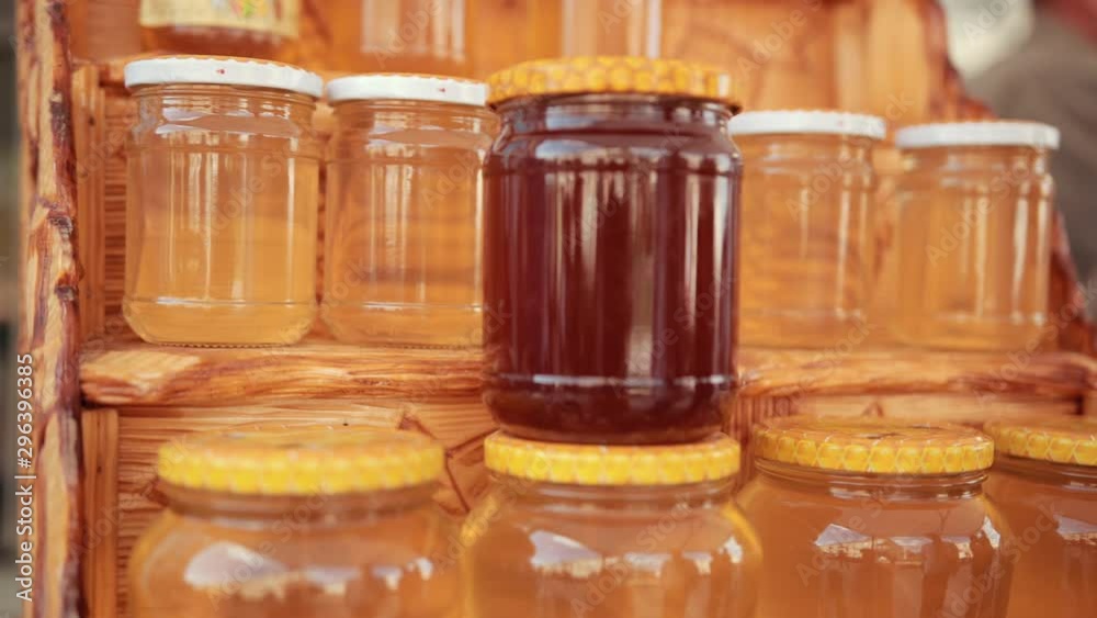 on wooden shelf there are many jars of honey, two kinds, closed with white and yellow lids, close-up, slow motion on wooden shelf there are many jars of honey, two kinds, closed with white and yellow lids, close-up, slow motion