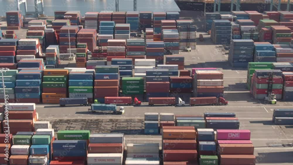 PORT OF LOS ANGELES, CALIFORNIA, UNITED STATES OF AMERICA, MARCH 2019: DRONE: Flying along a cargo truck hauling a container across the busy Port of Los Angeles. Truck navigates the industrial harbor.