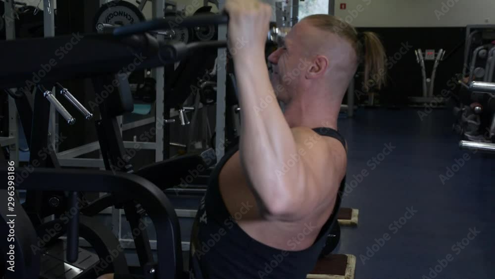 Side view of strong muscular bodybuilding man doing wide grip lat pulldown muscle repetition workout exercise in gym Side view of strong muscular bodybuilding man doing wide grip lat pulldown muscle repetition workout exercise in gym