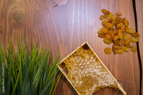 honey in combs next to raisins with green grass leaves on a wooden background