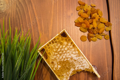 honey in combs next to raisins with green grass leaves on a wooden background