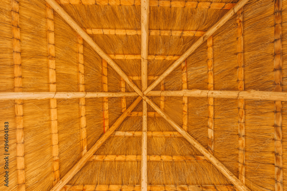 Close - up of the interior of the thatched roof with a crossbar. Use for backgrounds or textures with copy space. Thatched roof inside in the form of cobwebs . Sunny weather under the roof. Real straw