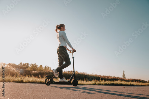 Young beautiful girl riding an electric scooter in the summer on the street, against the sunset, there is free space for advertising against the sky