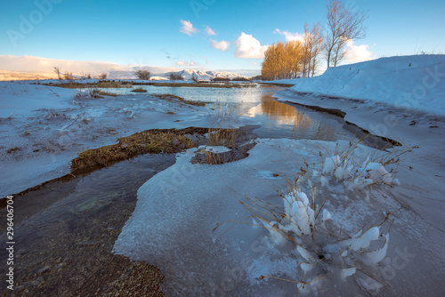 River flows through frozen field covered with snow