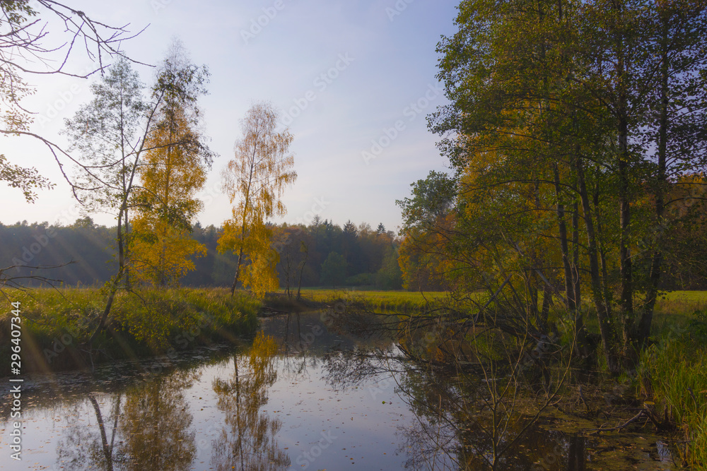 Fototapeta premium Autumn landscape before sunset. Lake water and grass fields in the distance trees, village, greenery