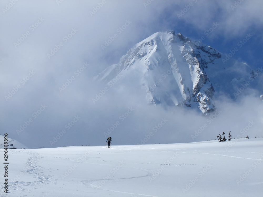 A lone backcountry skier makes his way up the Mt. Hood Cooper Spur route. Mt. Hood looms large through the clouds above the skier. He is earning his turns.